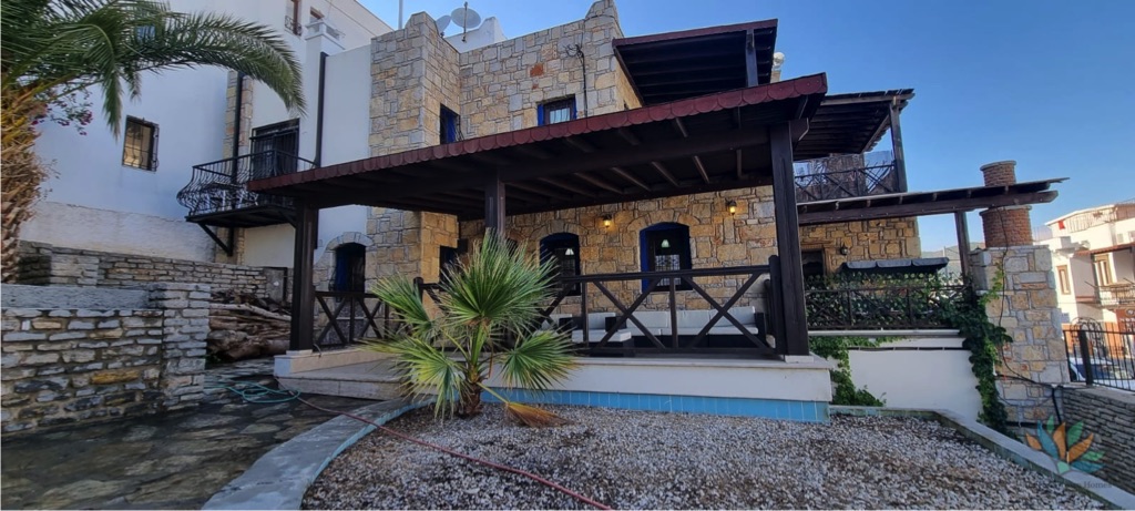 “Property listing photo: Photo shows a a stone villa for sale in Gumbet Bodrum with garden and trees.